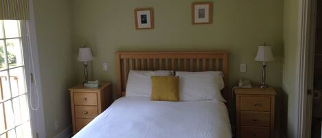 A bedroom with a large bed, two bedside tables with lamps, a wooden headboard, and two framed pictures on the wall.