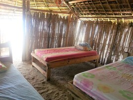 A room with a thatched roof, wooden bed frames, and a mattress with a floral print.