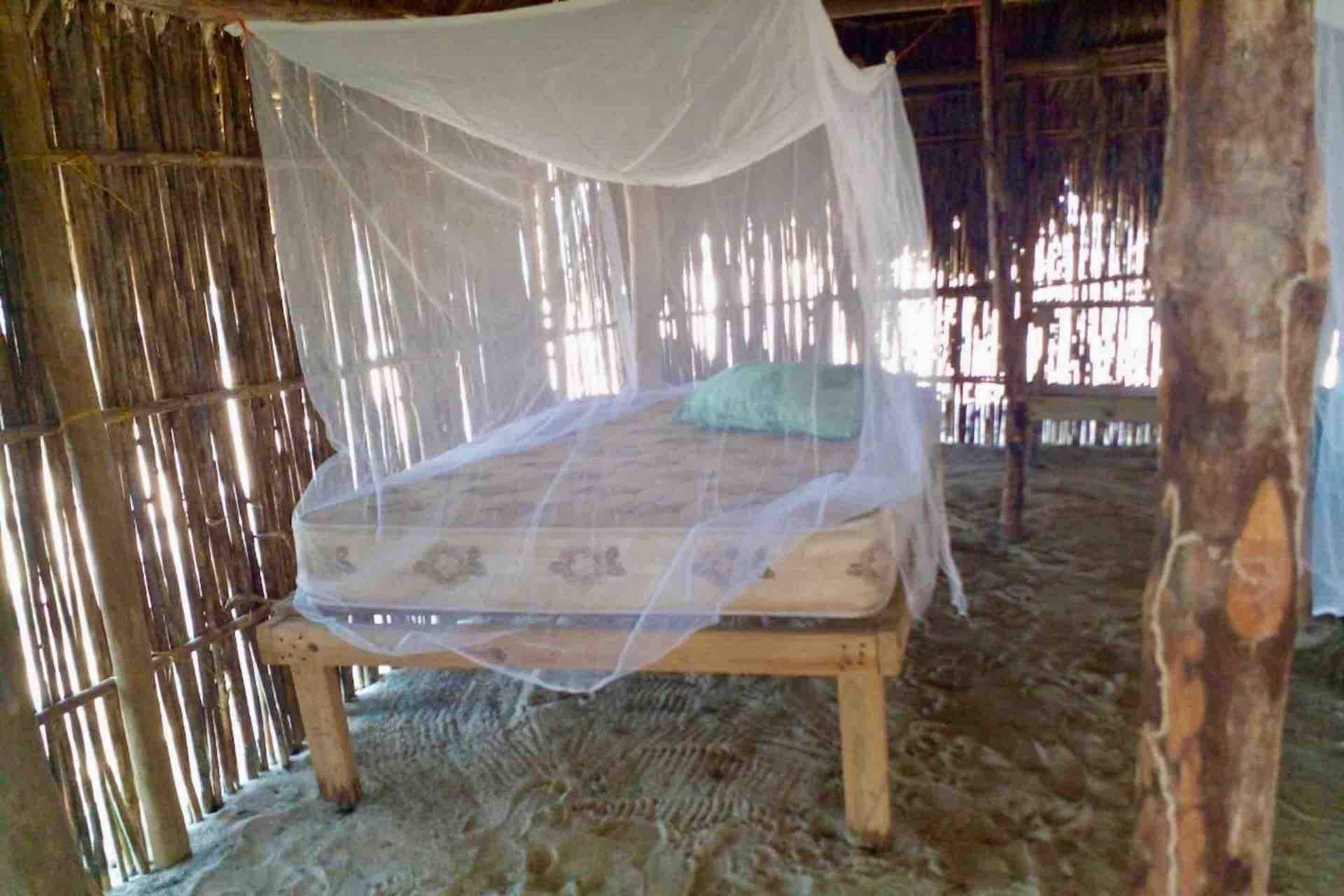 A bed with a mosquito net in a rustic room with bamboo walls.