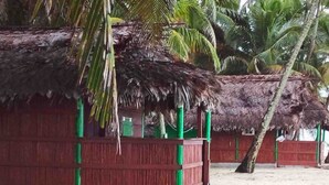 A thatched-roof hut with a wooden frame and green accents, situated on a sandy beach with palm trees in the background. - Cabins in Asserya Island - San Blas paradise - meals included (Ailigandi)