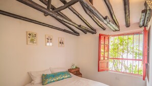 A bedroom with a bed, a nightstand, and a window with red bars. - Botanico Hostel (Bogotá)