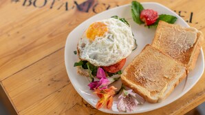 A plate with a fried egg, tomato, lettuce, and toast on a wooden table. - Botanico Hostel (Bogotá)