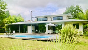 Et moderne hus med swimmingpool, store vinduer og en overdækket patio.