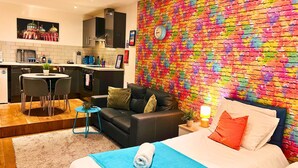 A modern hotel room with a black leather sofa, a bed with a blue blanket, and a colorful brick-patterned wall.