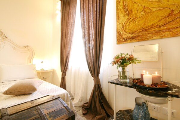 A bedroom with a bed, curtains, a vase with flowers, and a nightstand.