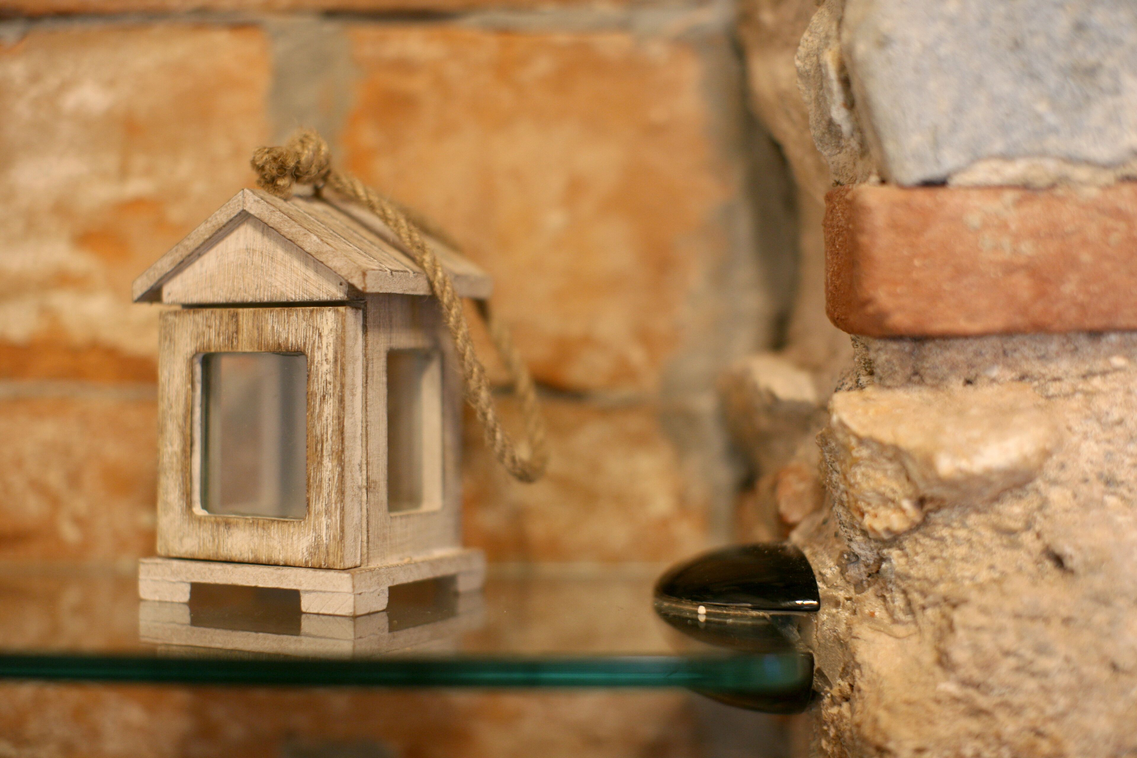 Un farol de madera sobre una repisa de vidrio frente a una pared de piedra.