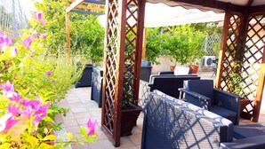 Une terrasse extérieure avec des meubles en osier, une pergola et des plantes en pot.