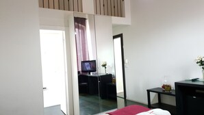 Une chambre d’hôtel moderne équipée d’un lit, d’un bureau avec un ordinateur, d’un miroir et d’une télévision.