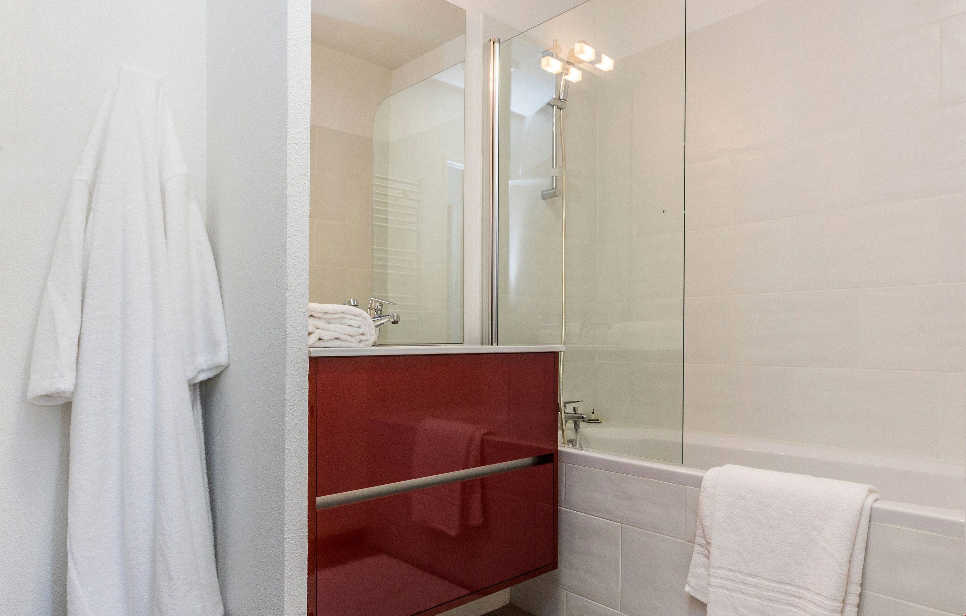 Une salle de bain moderne avec une douche à parois de verre, un meuble-lavabo rouge et une baignoire blanche.
