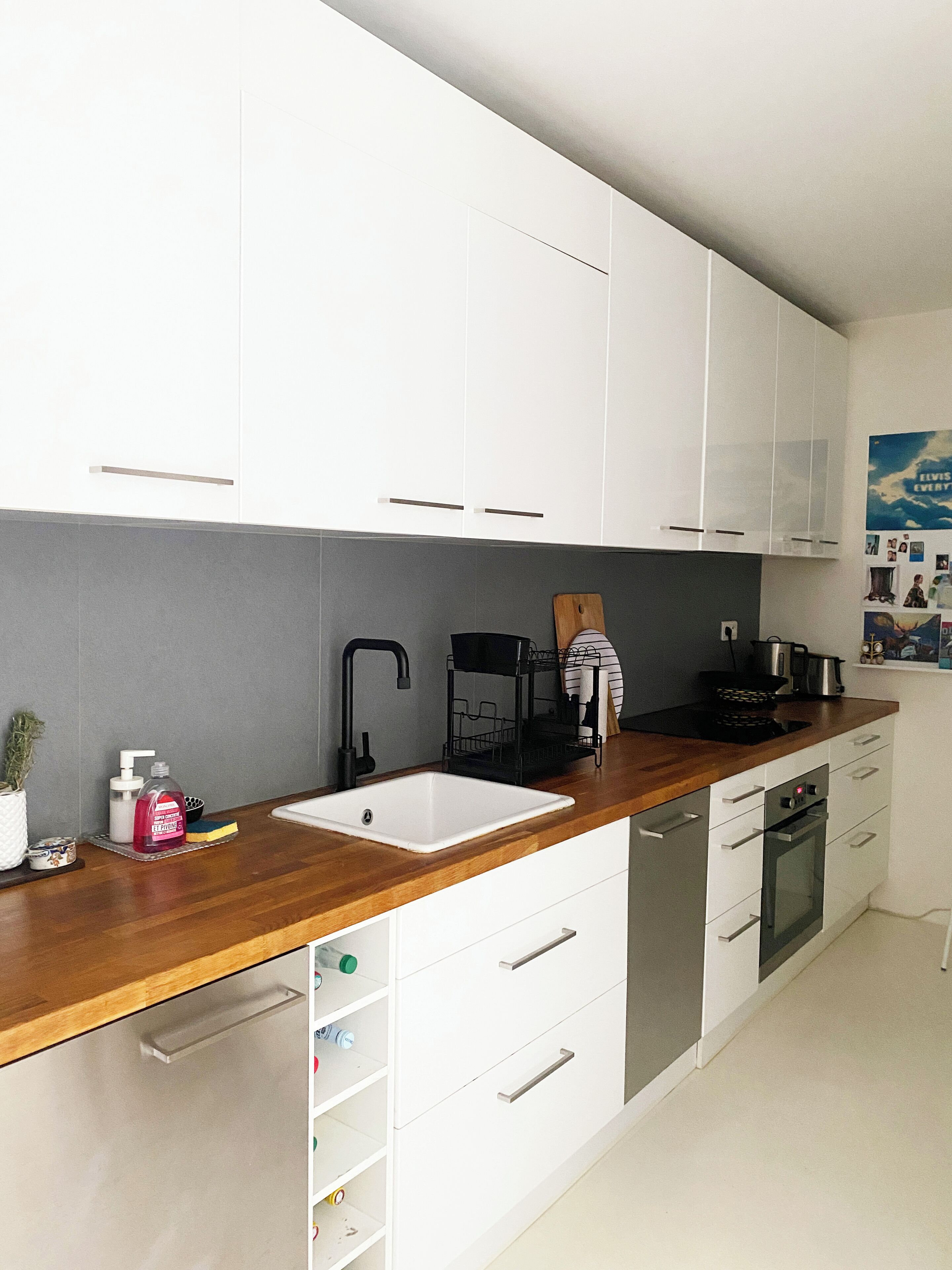 Une cuisine moderne avec des meubles blancs, un plan de travail en bois, un évier, une cuisinière et un lave-vaisselle.
