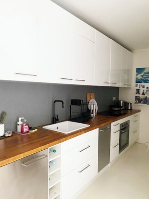 Uma cozinha moderna com armários brancos, bancada de madeira, pia, fogão e lava-louças.