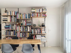 Quarto com uma grande estante de madeira cheia de livros, uma mesa de madeira e duas cadeiras.