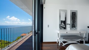 Un balcon avec vue sur la mer, un bureau blanc avec une chaise et un lit.