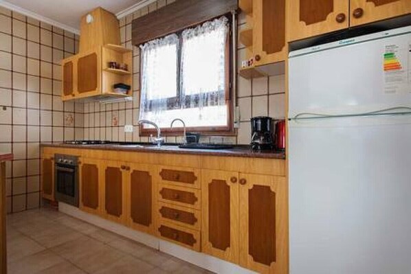 Une cuisine avec des meubles de rangement en bois, une cuisinière encastrée, un évier et un réfrigérateur.