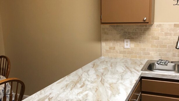 A kitchen with a marble countertop, wooden cabinets, a clock, and a decorative wall piece.