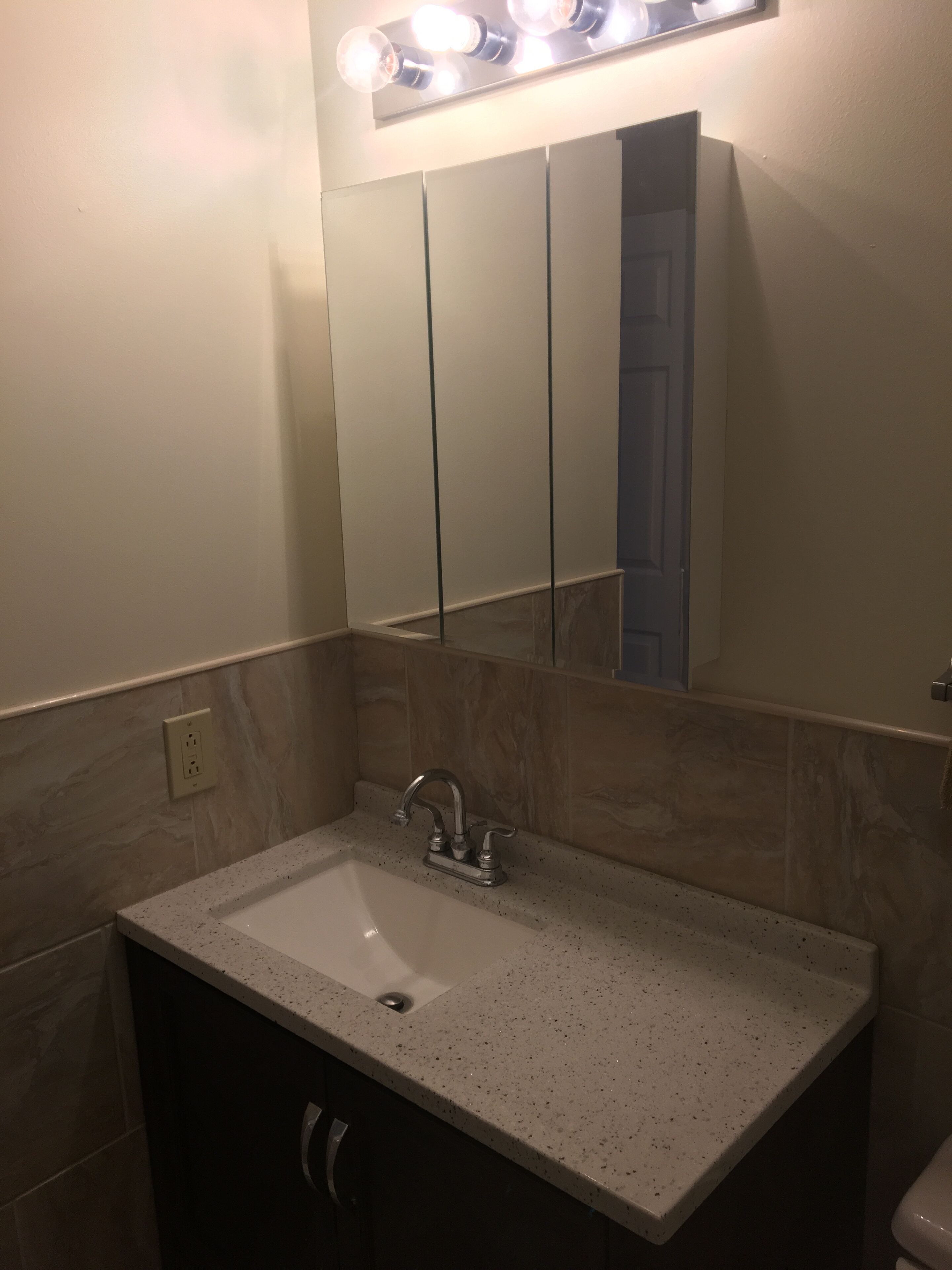 A bathroom with a white sink, a mirror above it, and a light fixture above the mirror.