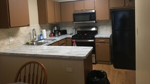 A kitchen with wooden cabinets, a stainless steel microwave, a gas stove, and a black refrigerator.
