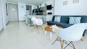 Ein modernes Wohnzimmer mit einer Couch, zwei weißen Sesseln, einem Couchtisch und einer Küchenzeile mit Esstisch.