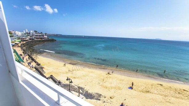 Une plage avec une eau cristalline, un rivage sablonneux et des bâtiments en arrière-plan.