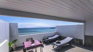 Un balcon avec une table, des chaises et des fauteuils, donnant sur la mer.