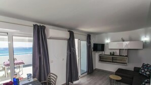 Un salon moderne avec un canapé, un téléviseur, une table à manger et des chaises, et une vue sur la mer grâce à de grandes fenêtres.