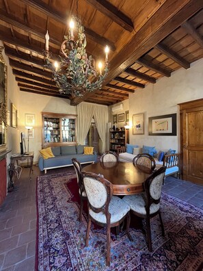 A dining area with a wooden table and chairs, surrounded by a patterned rug, with a chandelier above. - Garibaldi Suite - Turin's downtown - Turin center (Torino)