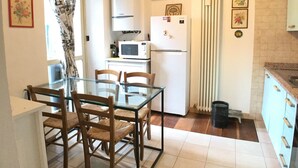 A kitchen with a dining table and chairs, a microwave, a refrigerator, and a shelf with bottles. - Garibaldi Suite - Turin's downtown - Turin center (Torino)