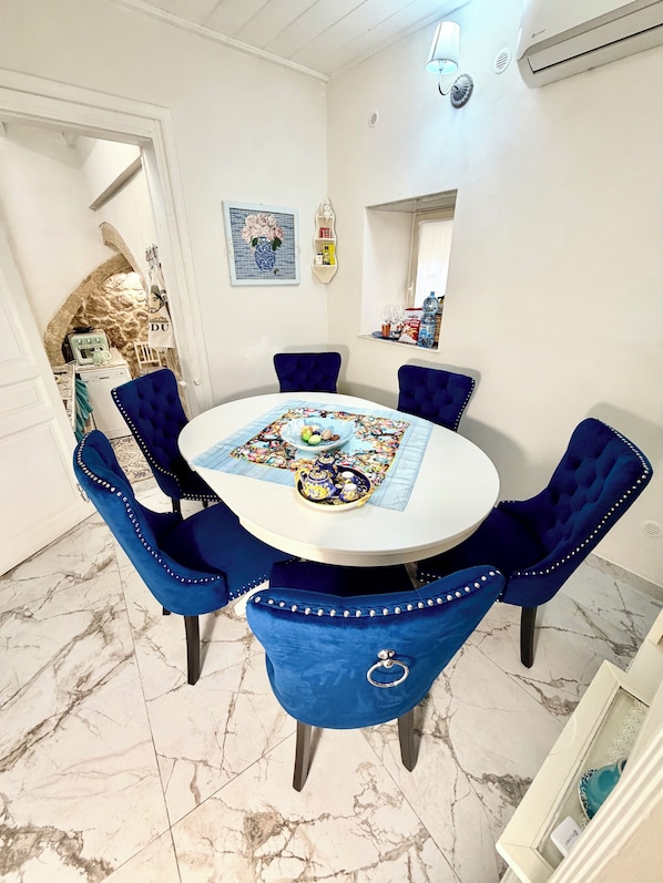 Un coin repas avec une table ronde, des chaises à revêtement bleu, un chemin de table décoratif et une arche en pierre menant à une autre pièce.