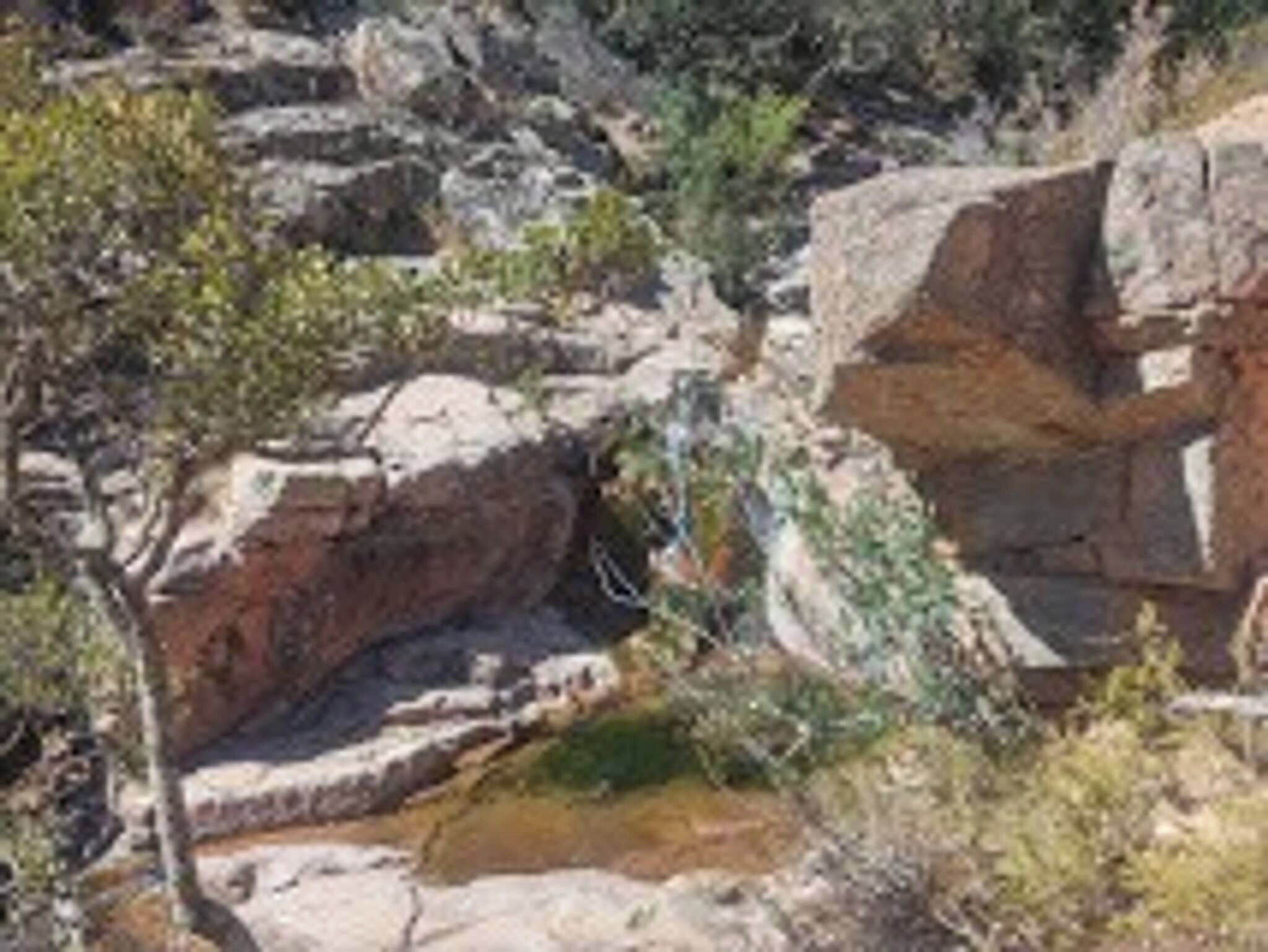 A rocky landscape with a large boulder and sparse vegetation.