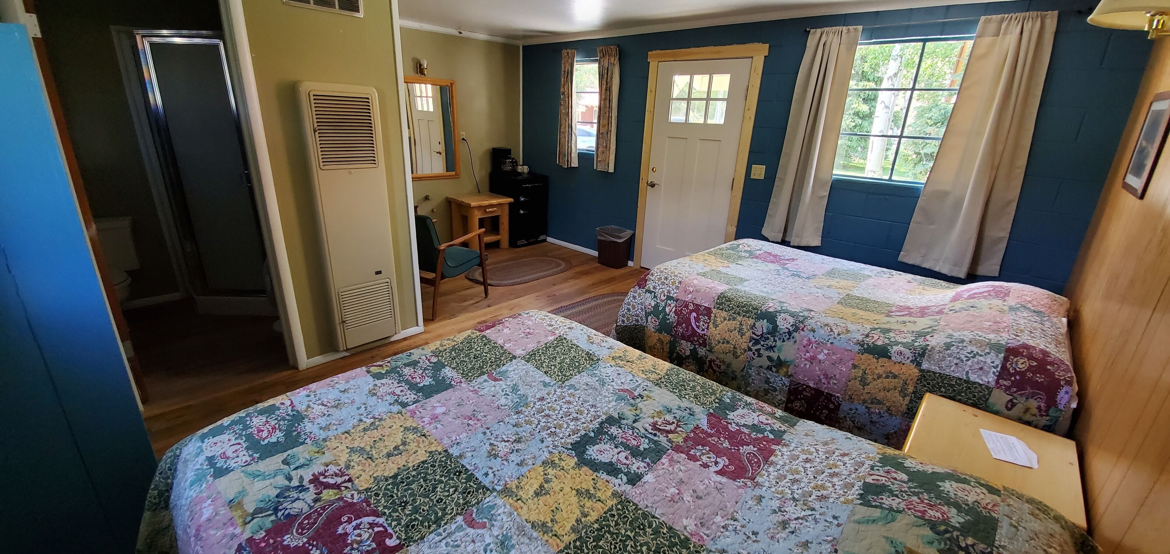 Une chambre avec deux lits, un bureau, une chaise, un miroir et une porte.