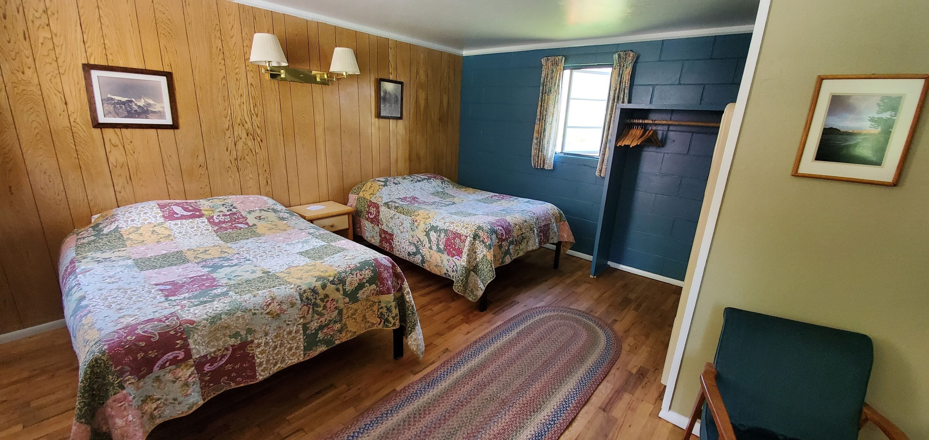 Une chambre avec deux lits, des murs en bois, une fenêtre avec des rideaux et une petite table.