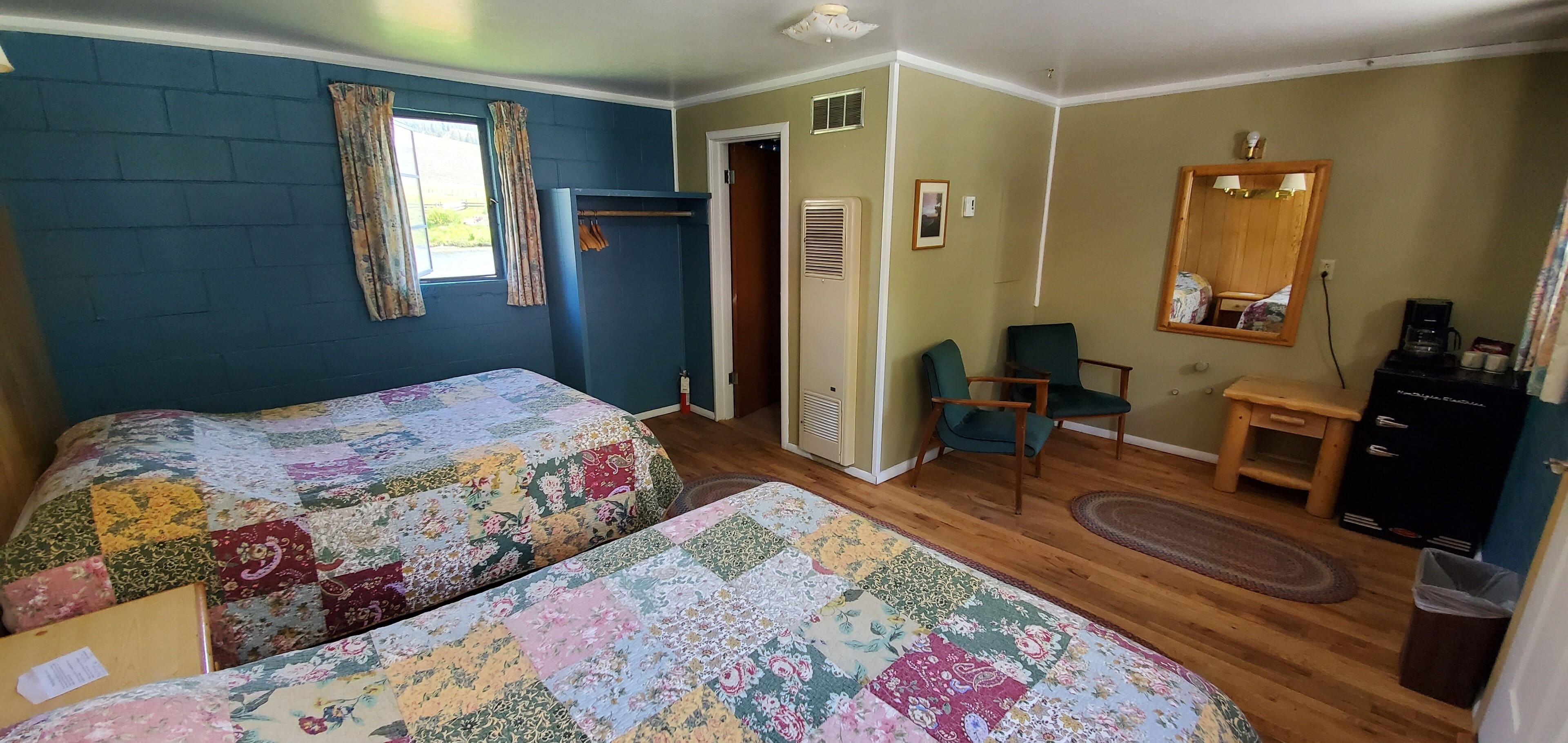 A room with two beds, a chair, a small table, a mirror, and a heater.