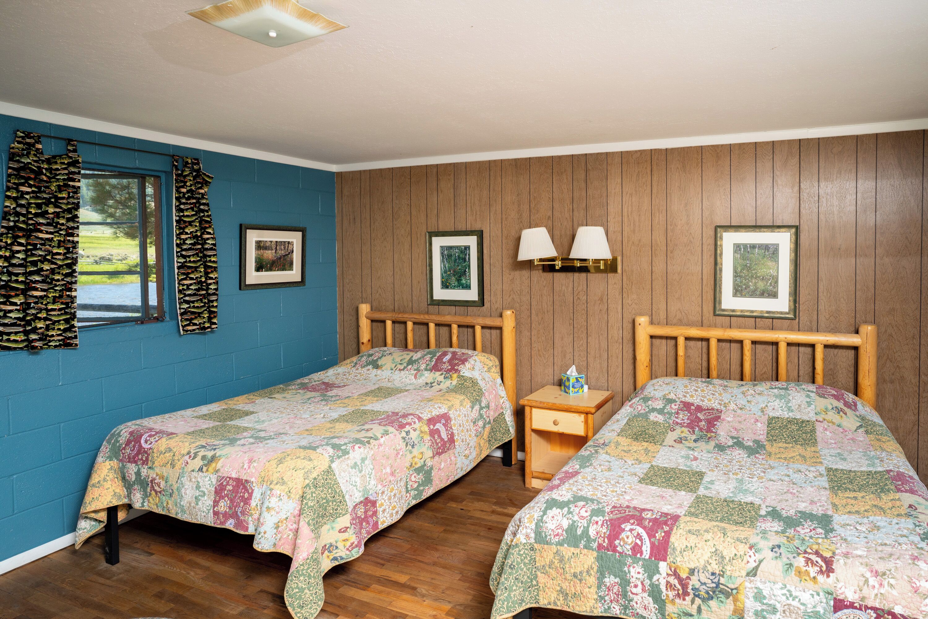 Une chambre avec deux lits en bois, une table de chevet et une fenêtre avec des rideaux.