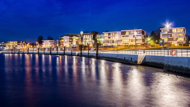 Ett hotell vid vattnet med modern arkitektur, en spegelblank pool och balkonger med belysning.