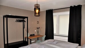 Ett sovrum med en säng, ett skrivbord, en hängande lampa och ett fönster med gardiner.