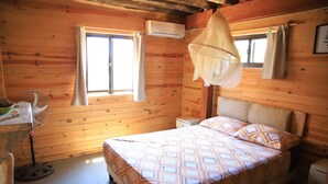 A wooden cabin bedroom with a bed, an air conditioner, a fan, and a window with curtains. - mandalas demar (Punta del Diablo)
