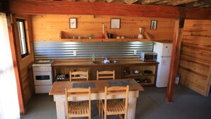A compact kitchen with wooden cabinets, a built-in microwave, a sink, and a stove. There are two wooden chairs around a small table. - mandalas demar (Punta del Diablo)