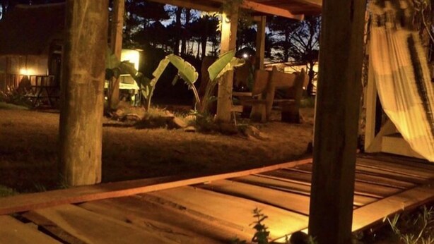 A wooden deck with a pergola structure, surrounded by trees and a building in the background. - mandalas demar (Punta del Diablo)