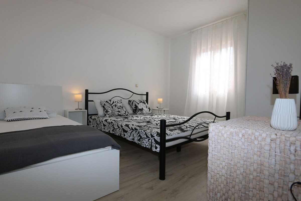 Ein Schlafzimmer mit zwei Betten, einem Nachttisch mit Lampe, einem Sessel und einer Vase mit Blumen.