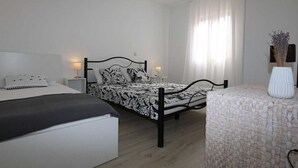 Un dormitorio con dos camas, una mesita de noche con lámpara, una silla y un florero con flores.