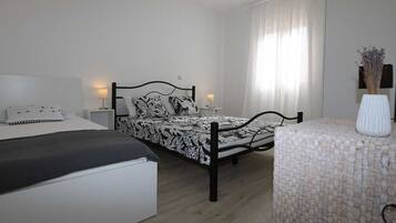 Ein Schlafzimmer mit zwei Betten, einem Nachttisch mit Lampe, einem Sessel und einer Vase mit Blumen.