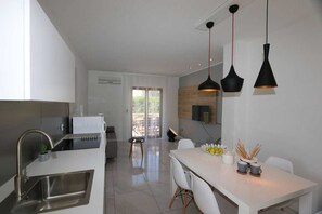Cozinha moderna com pia de aço inoxidável, área de refeições com mesa e cadeiras brancas e luminárias pendentes.
