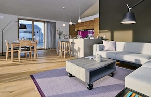 A modern living room with a grey sofa, a wooden dining table with chairs, a coffee table with wheels, and pendant lights.