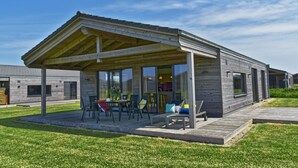 Una casa moderna con un porche cubierto, un comedor y una cocina visibles a través de puertas de vidrio.