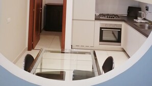 A compact kitchen with white cabinets, a gas stove, and a sink. There is a dining area with a glass table and chairs. - Da Bianca Apartment in Siena (Siena)