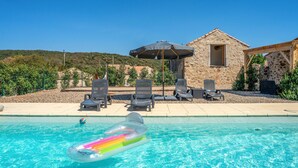 Ein Poolbereich mit Liegestühlen, einem Sonnenschirm und einem dahinterliegenden Steinhaus.