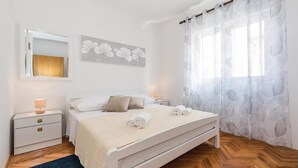 A bedroom with a bed, bedside tables, a mirror, and a window with sheer curtains. - 3 bedroom stunning apartment in Sibenik (Sibenik)