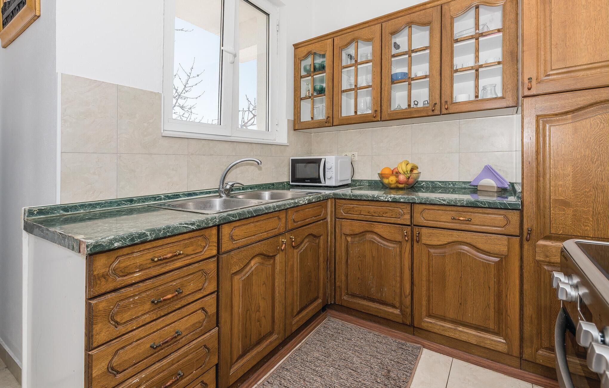 A kitchen with wooden cabinets, a granite countertop, a microwave, and a fruit bowl.