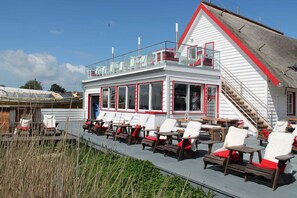 A building with a white exterior and red trim, featuring a balcony with chairs and tables.