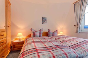 A bedroom with a bed, two bedside tables, a wooden wardrobe, a framed picture on the wall, and a window with curtains.